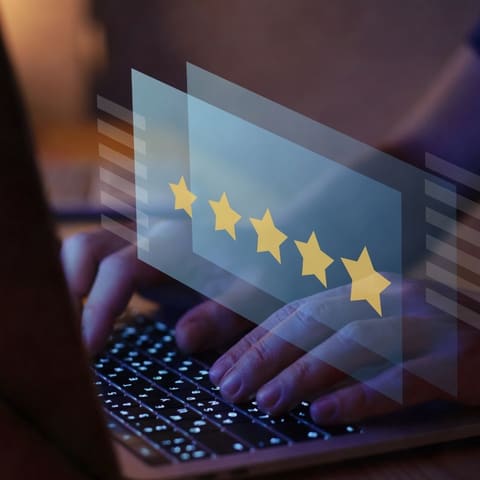 Hands typing on a laptop keyboard beneath five glowing gold rating stars